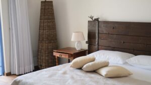 un letto con testata in legno massiccio di colore scuro, con lenzuola e copriletto chiaro